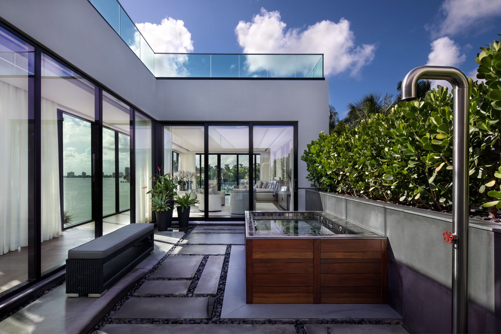 Terrace with a wood-clad cold plunge, stainless outdoor shower and glass walls looking into the living area