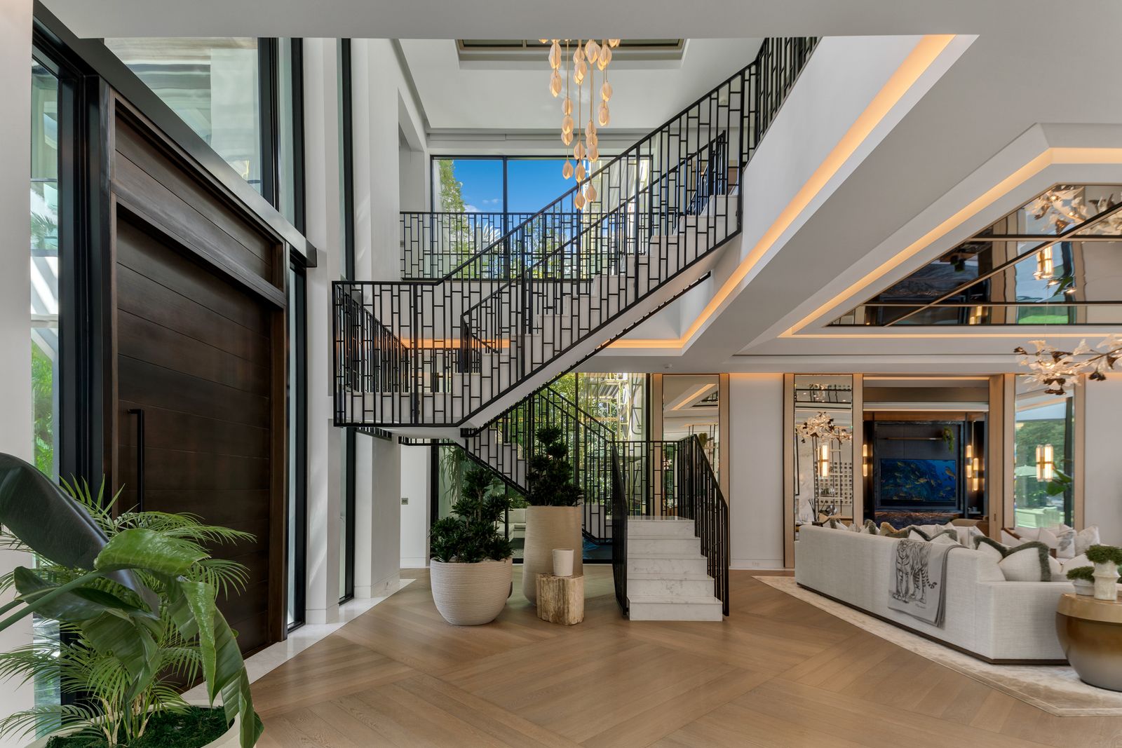 Double-height foyer with a sculptural black metal staircase, oversized wood entry door and herringbone floors