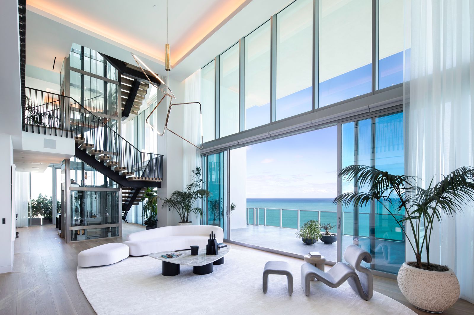 Double-height oceanfront condo living room with a floating staircase, glass elevator and floor-to-ceiling windows