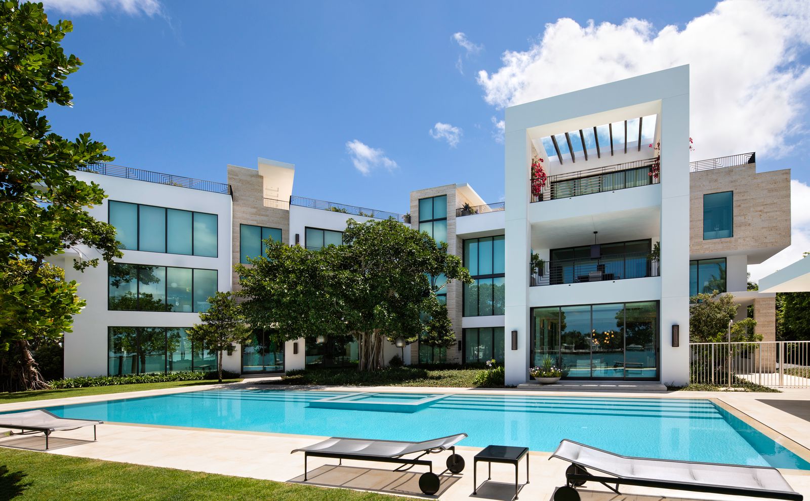 Three-story contemporary home by Bart Reines Luxury Homebuilder, with stone accents, a large pool and loungers