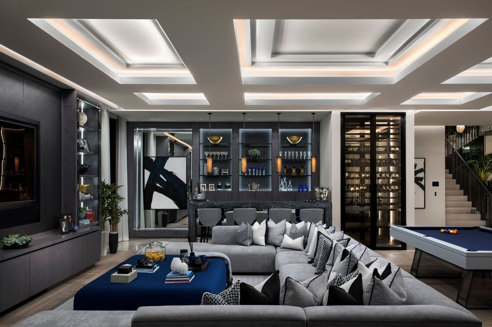 Entertainment lounge with a grey sectional, navy ottoman, glass wine room, bar display and billiards table