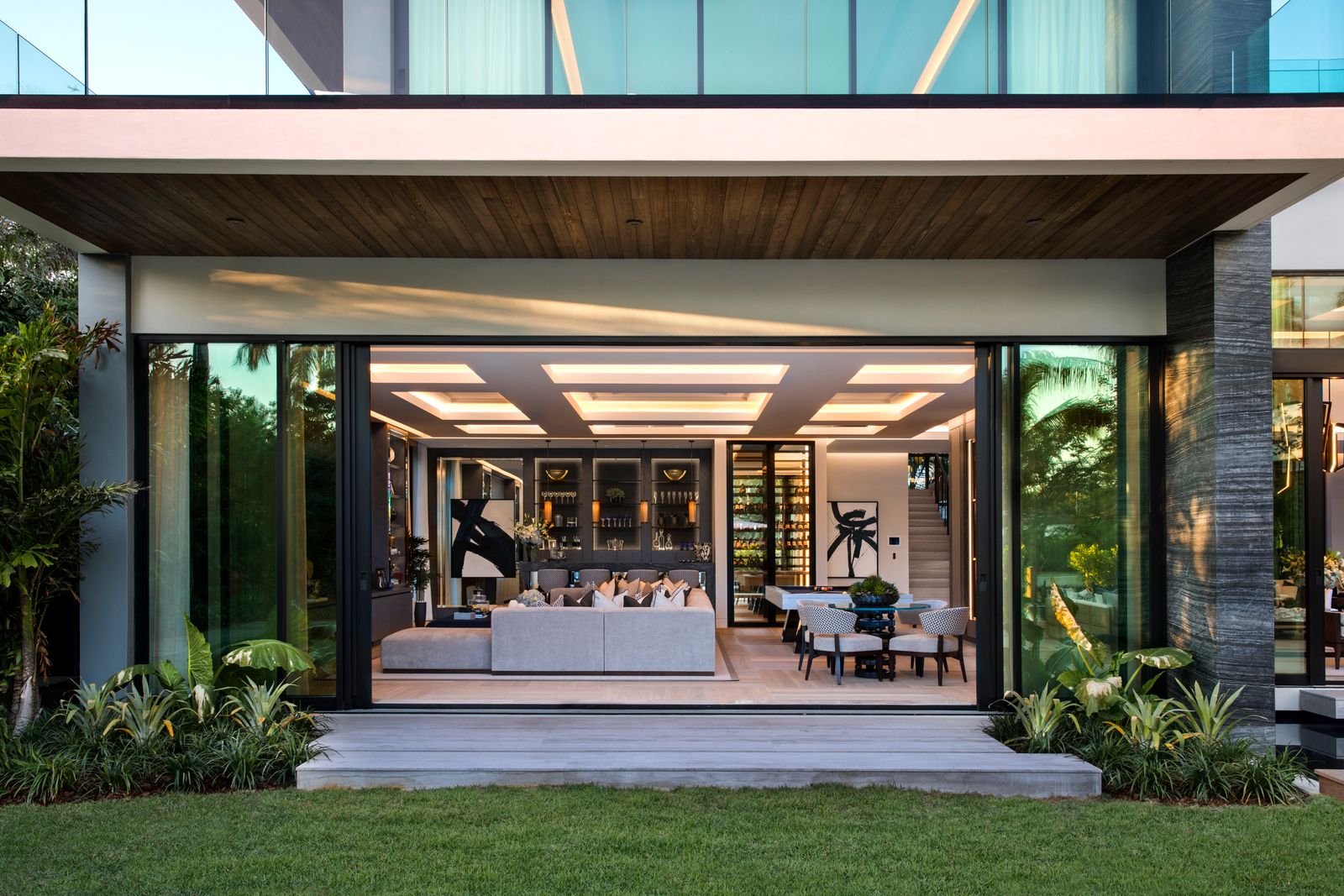 Rear facade with wall-to-wall glass doors open to a lounge, bar and dining area under a wood-clad overhang